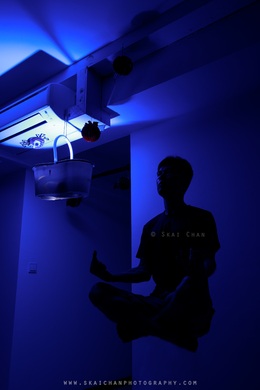 Silhouette of Skai floating in a meditation pose beneath the stained cooling unit, with a suspended blue-lit bucket